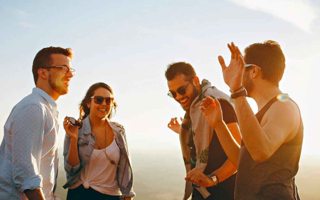 Un gruppo di giovani amici che ride e si diverte all'aperto in una giornata di sole, indossando occhiali da sole e abbigliamento casual, rappresentando il tema del vizio del bere tra i giovani